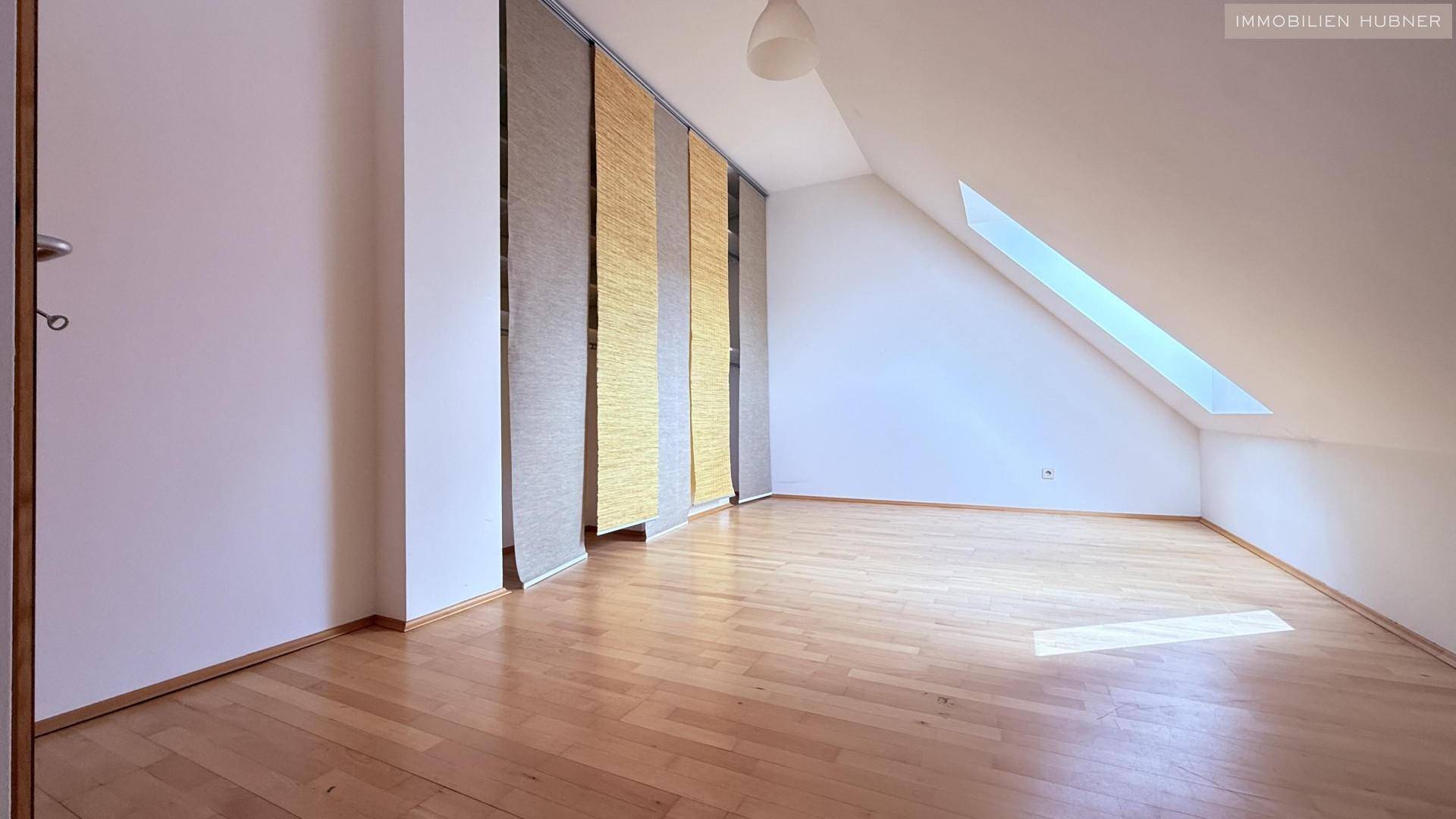 Helles Schlafzimmer mit Holzboden, Dachschräge und einem großen Dachfenster.