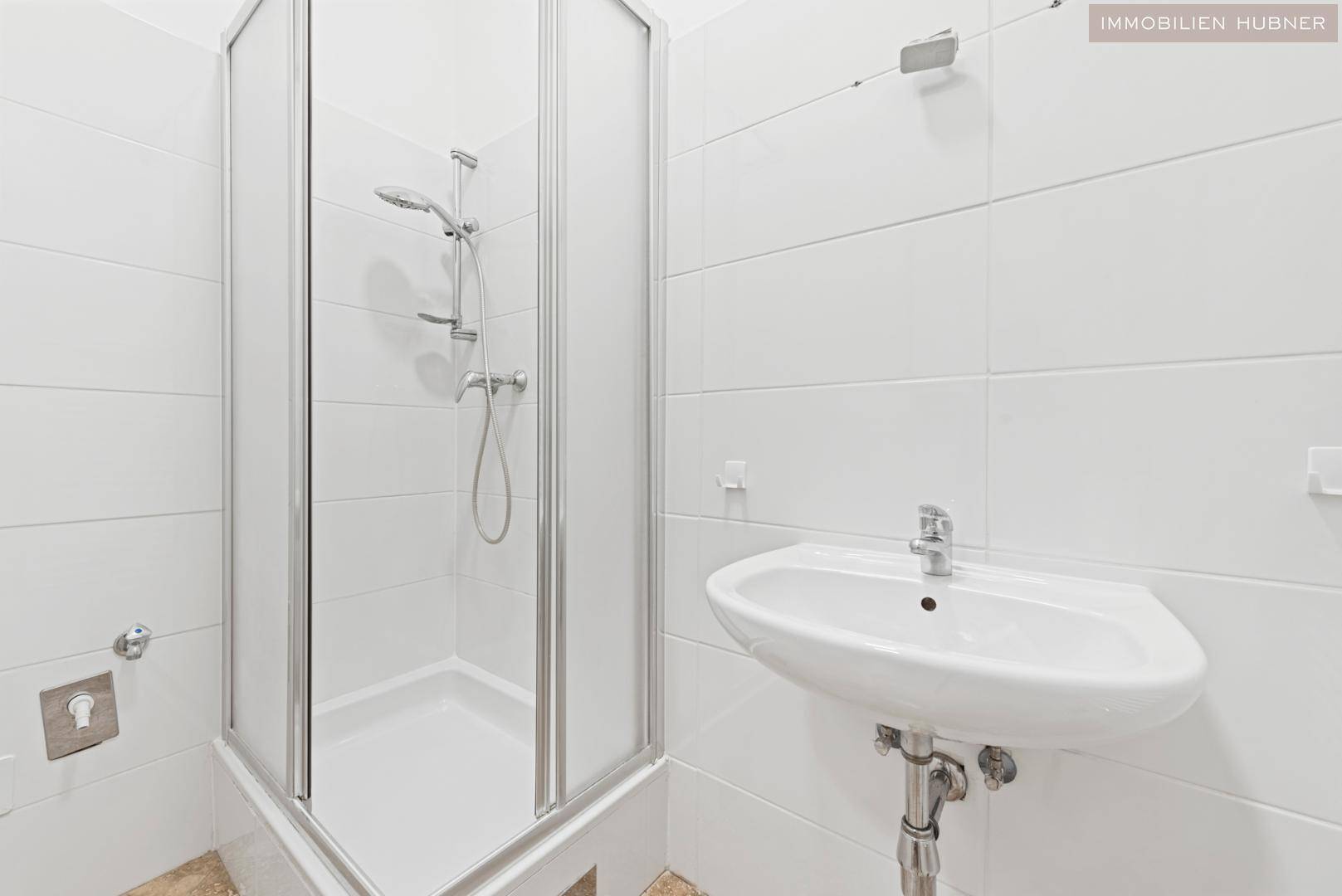Kleines Badezimmer mit weißen Fliesen, Duschkabine und einem Waschbecken.