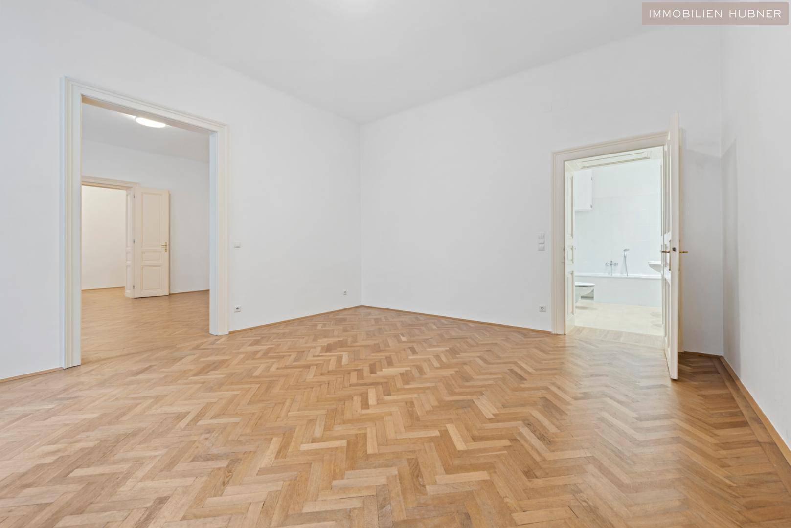 Geräumiges Zimmer mit Fischgrätparkett und direktem Zugang zu einem Badezimmer mit Badewanne.
