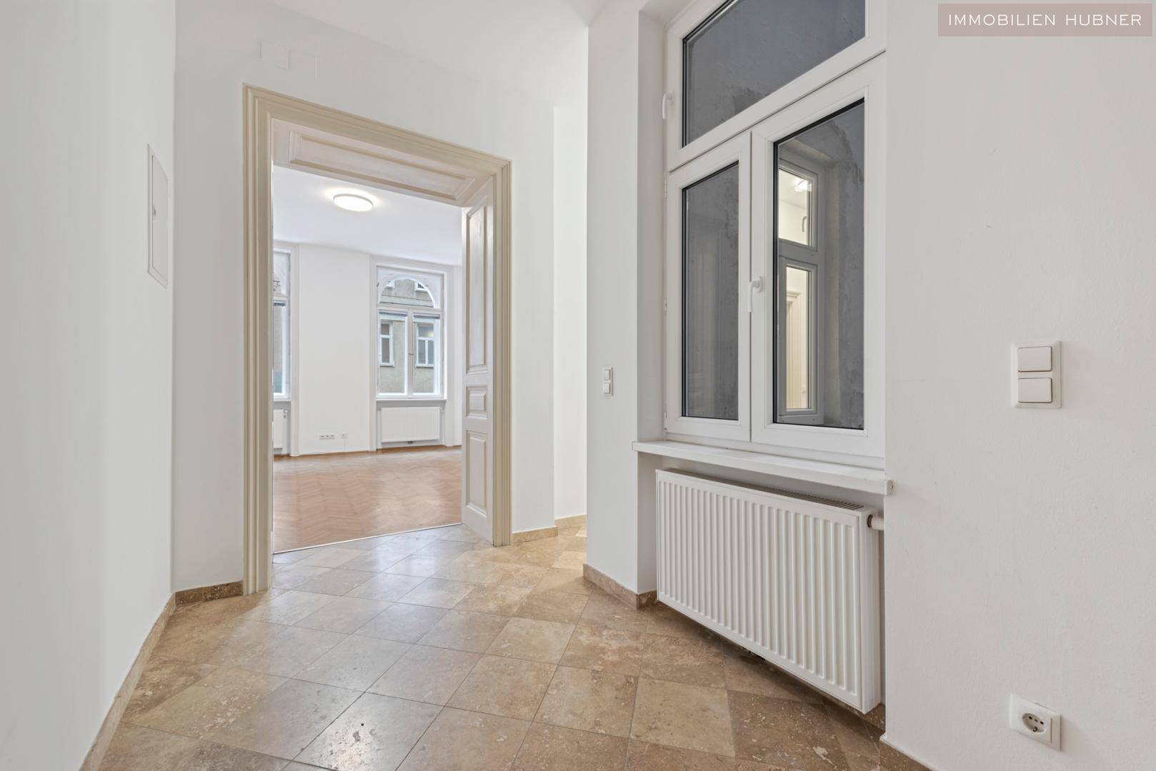 Geräumiger Flur mit Fliesenboden und einem Durchgang zu einem Zimmer mit Parkettboden.