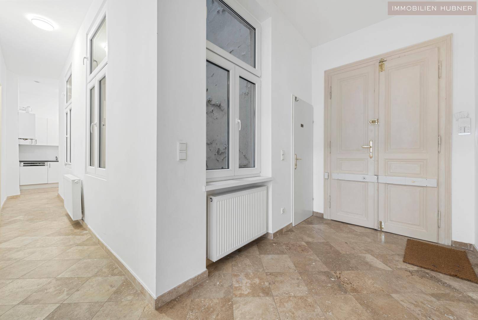 Heller Flur mit Fliesenboden, hohen Fenstern und einer Doppeltür, die in die Wohnung führt.
