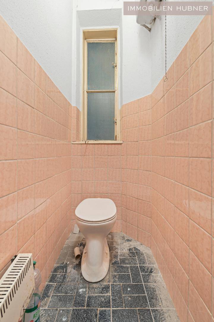 Kleines WC in Renovierung mit rosa Fliesen und Fenster, benötigt eine Modernisierung.
