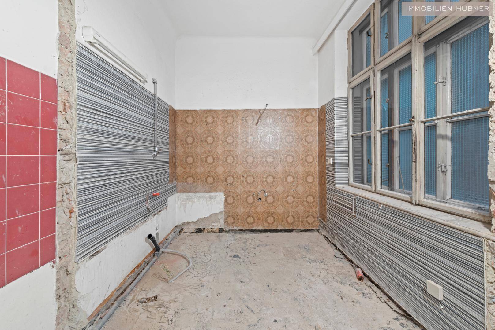Renovierungsbedürftige Küche mit alten Fliesen und Fenster, bietet Potenzial für Umbau.