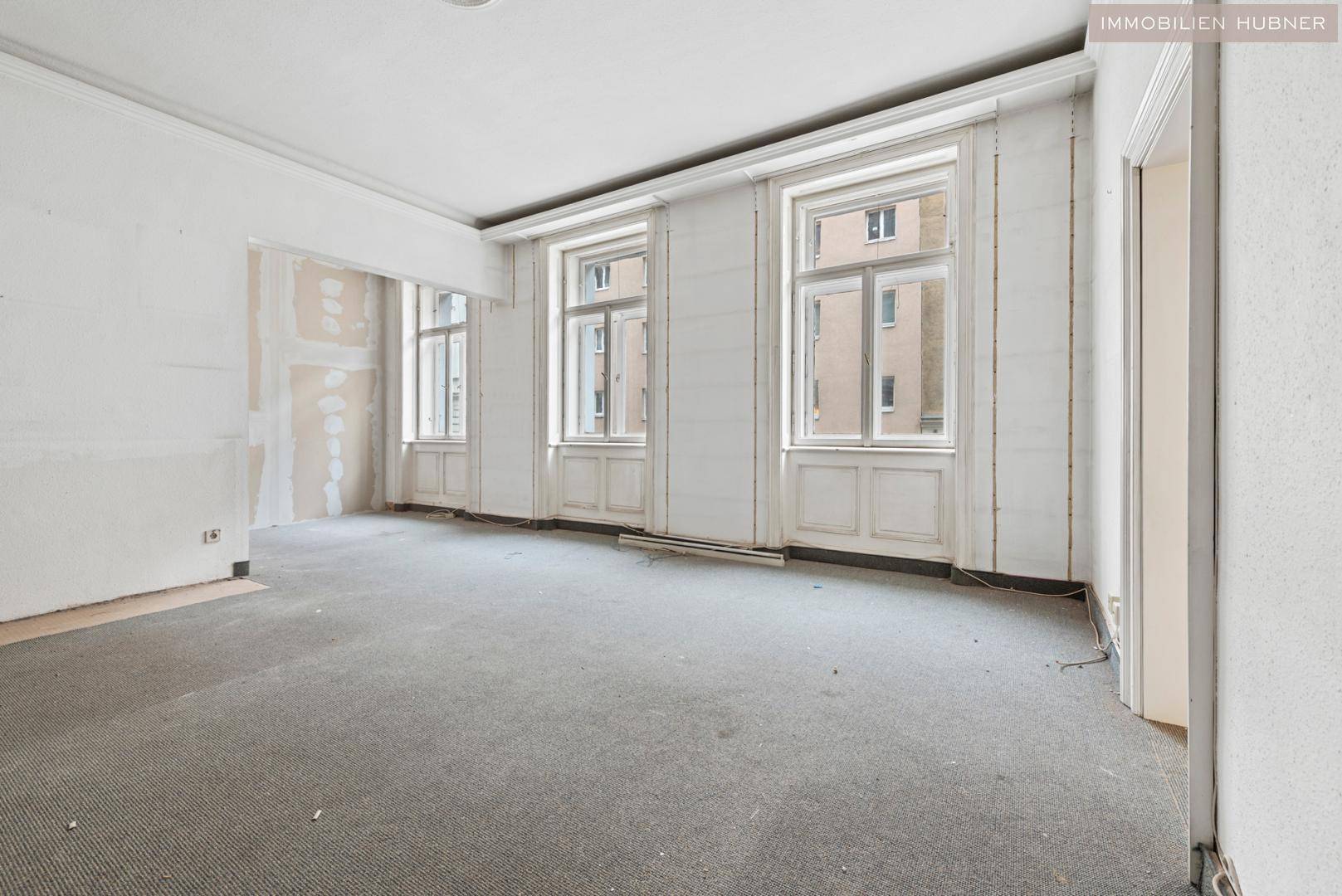 Heller Raum in Renovierung mit hohen Fenstern und Teppichboden, bereit für den Ausbau.