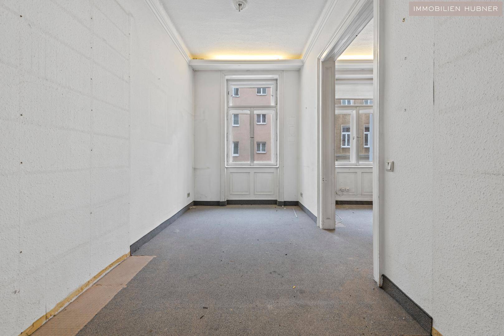 Weiterer Raum in sanierungsbedürftigem Zustand mit hohen Decken und Fensterblick.