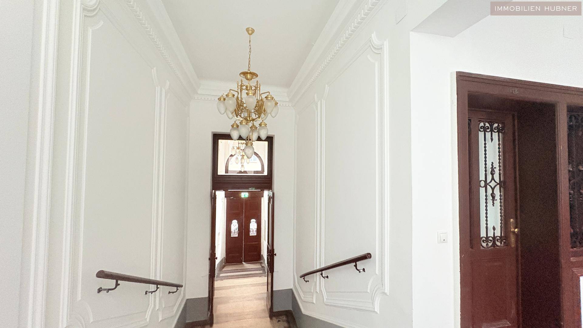 Elegantes Treppenhaus mit Stuckverzierungen, Kronleuchter und Holztüren im Altbau.