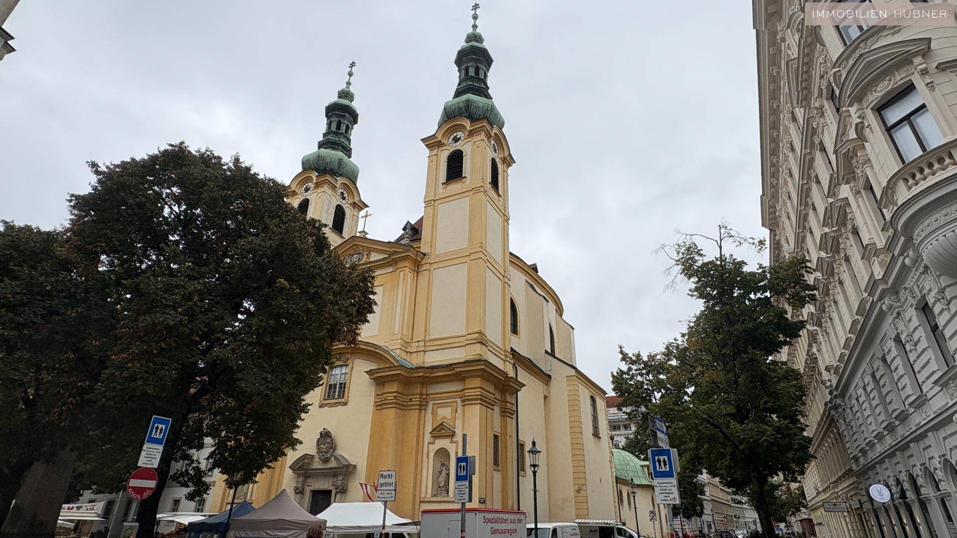 Historische Kirche mit zwei Türmen an einer Straße mit Bäumen und Gebäuden.