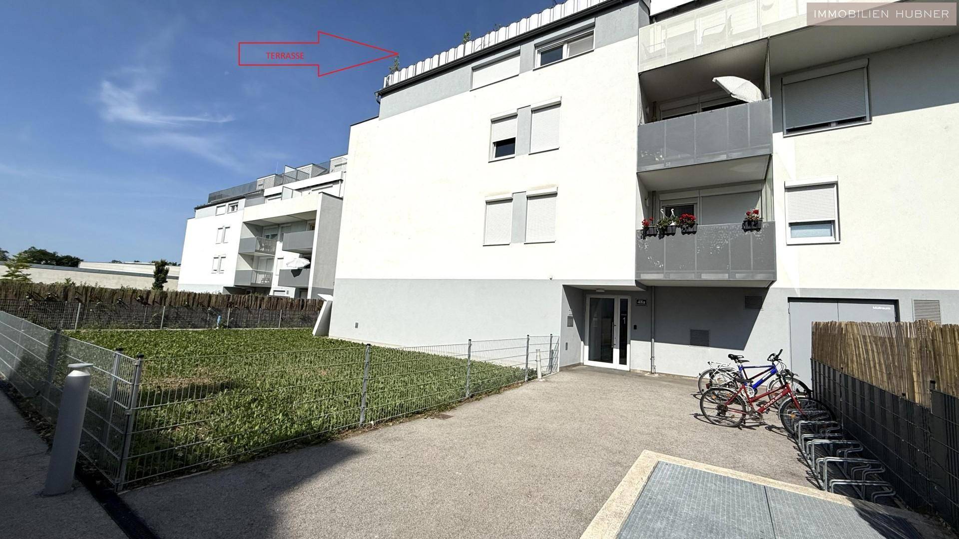 Seitenansicht eines modernen Apartmentgebäudes mit Balkonen und Fahrradabstellplatz im Freien.