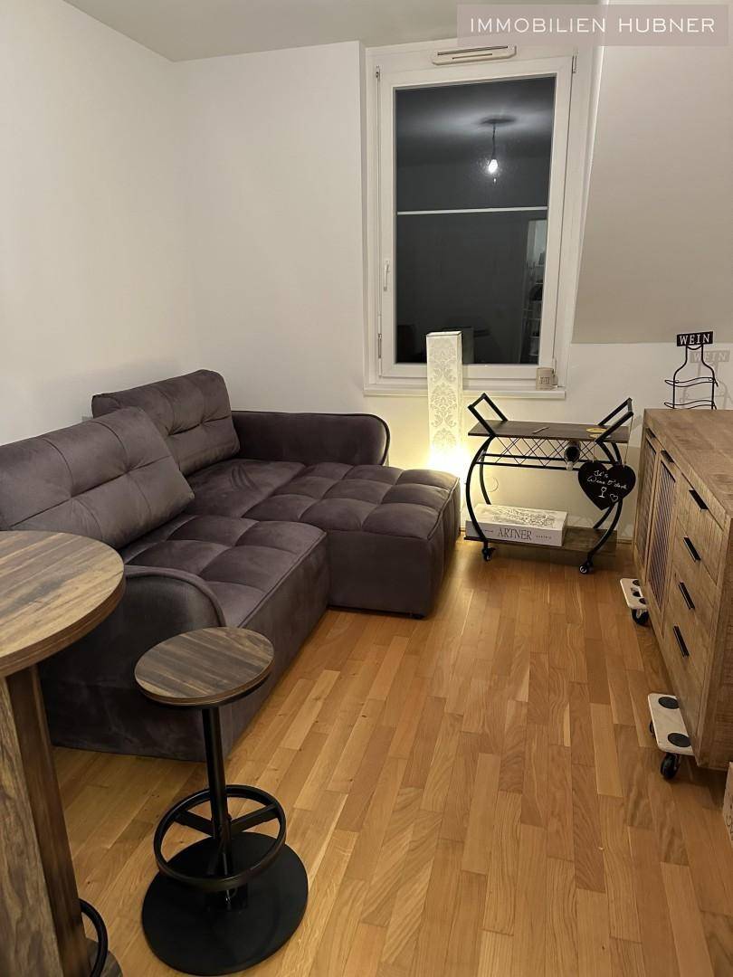 Gemütliches Wohnzimmer mit Ecksofa, Bartisch und Holzmöbeln, beleuchtet durch eine Stehlampe.