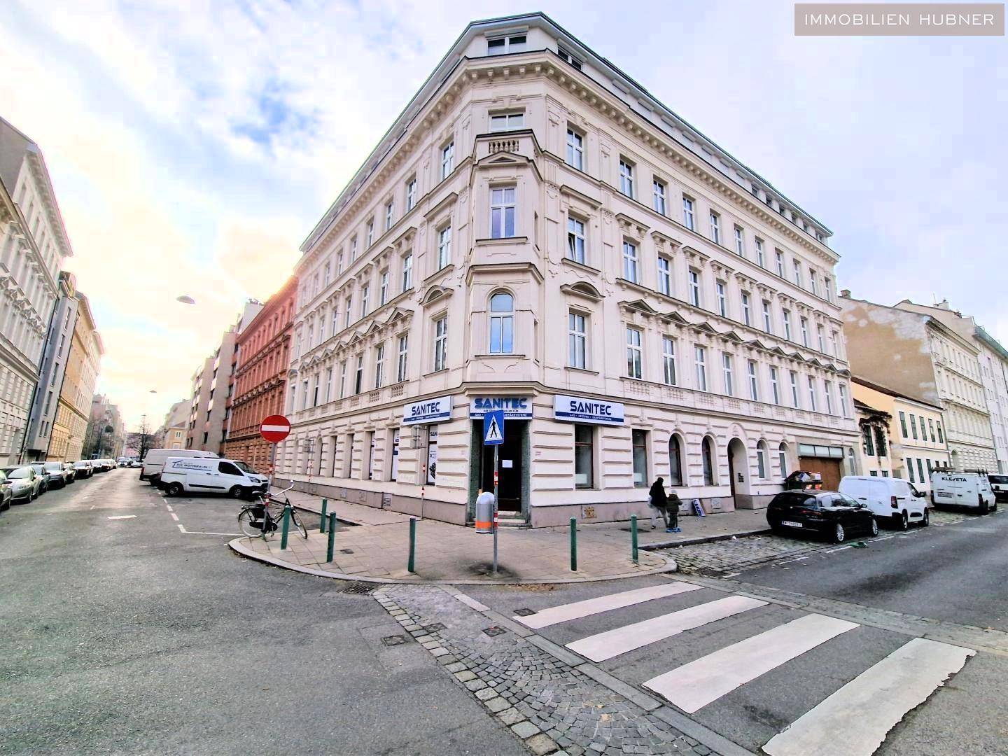 Historisches Eckgebäude in der Stadt mit klassischer Architektur und Geschäften im Erdgeschoss.
