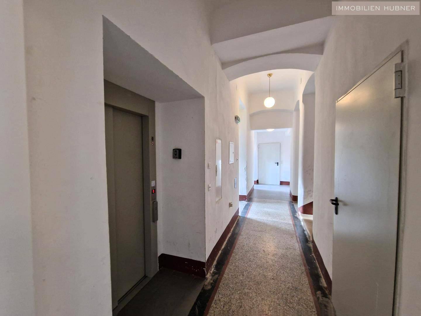 Langer Flur in einem Altbau mit Aufzug und Terrazzoboden, der zu den Wohnungen führt.