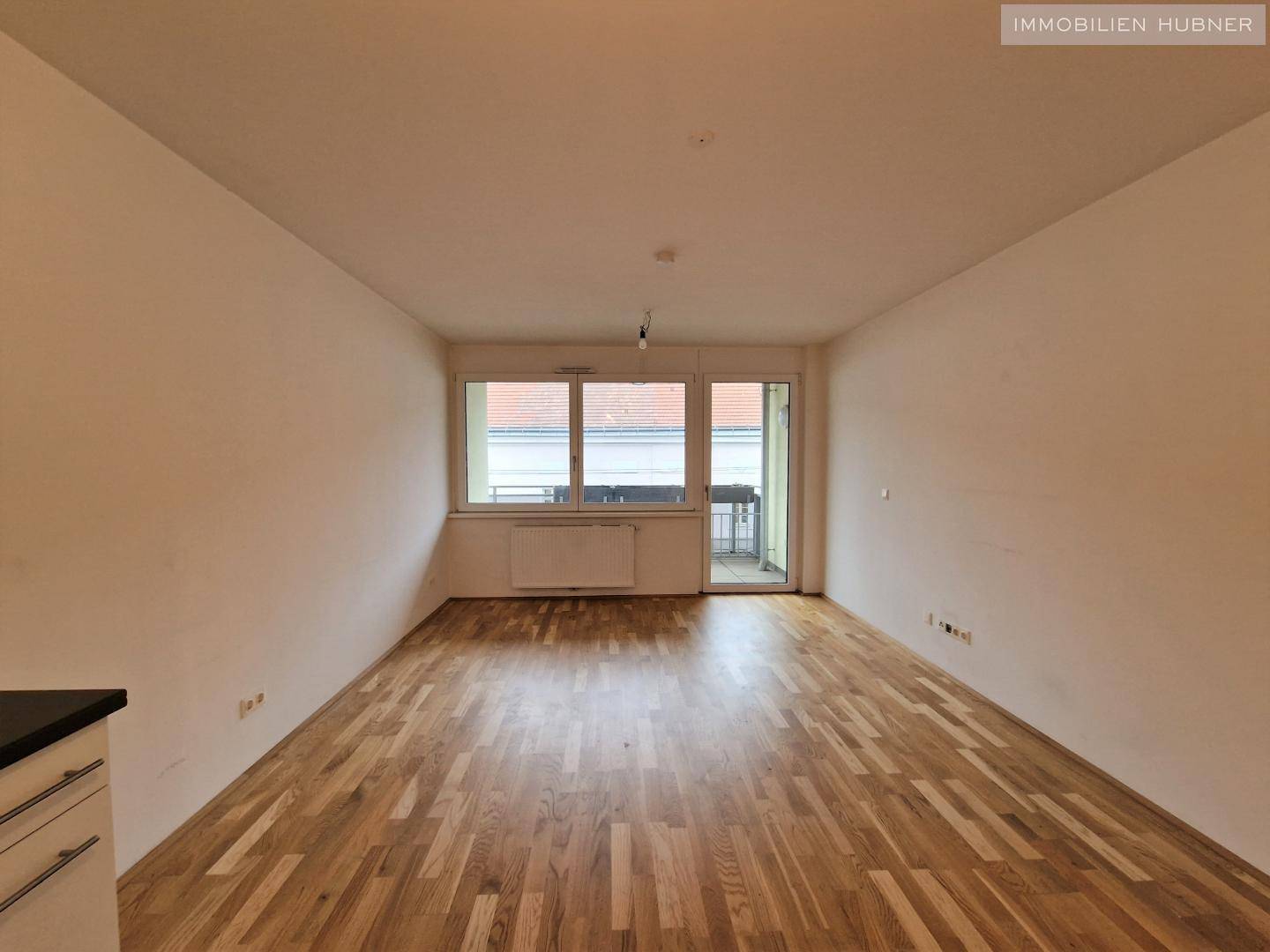 Geräumiges Wohnzimmer mit Parkettboden und großen Fenstern, die viel Licht hereinlassen.