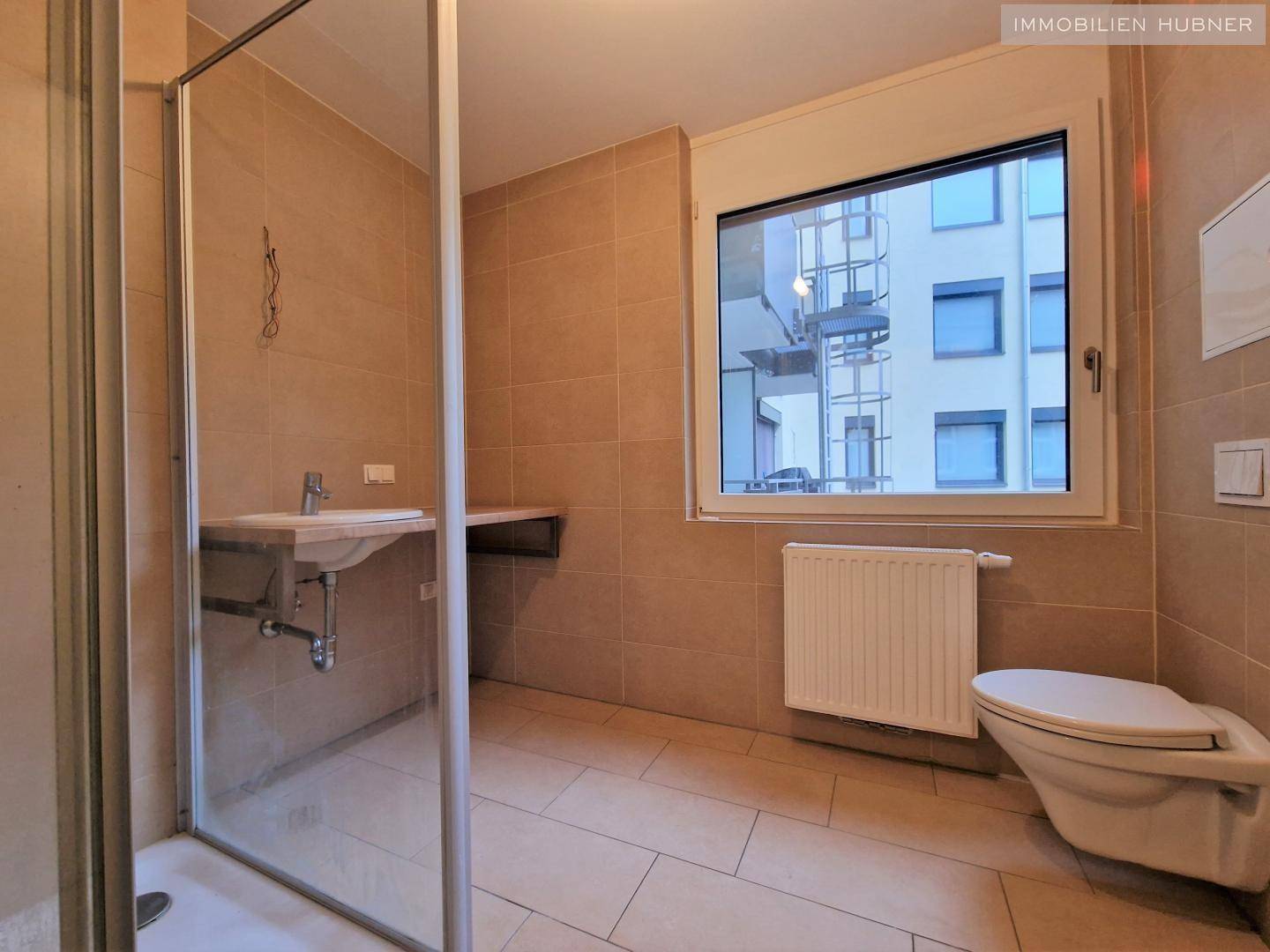 Gefliestes Badezimmer mit Dusche, WC und Fenster für natürliche Belüftung.
