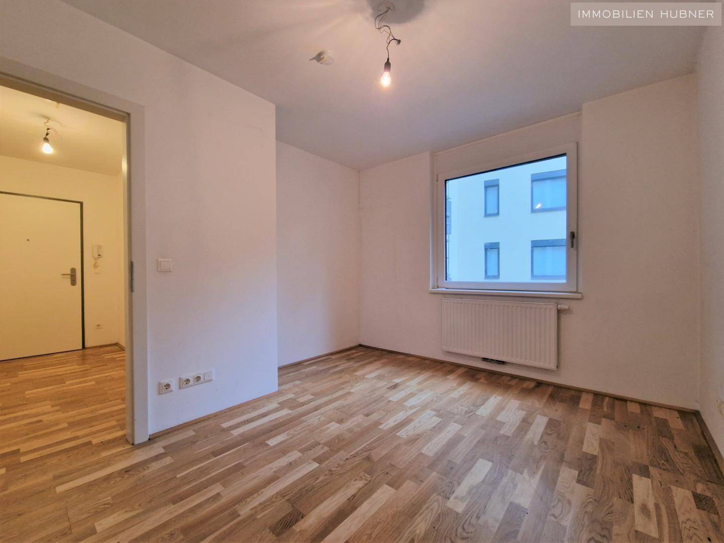 Helles Schlafzimmer mit Parkettboden und großem Fenster, bereit zur individuellen Gestaltung.