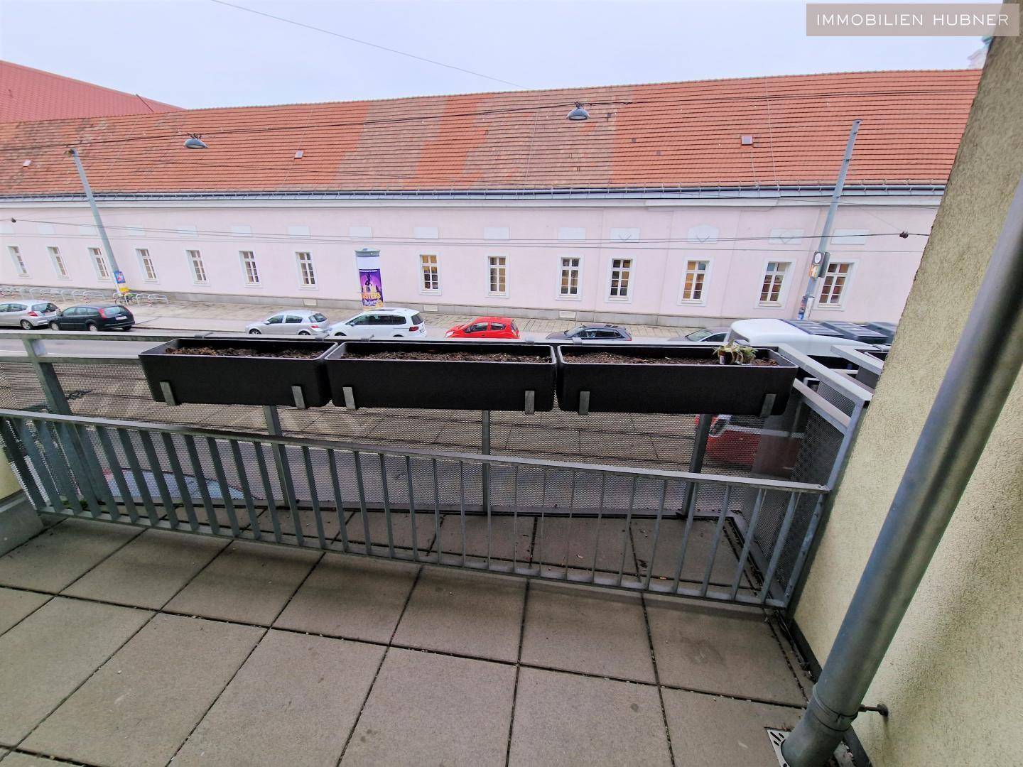 Balkon mit Fliesenboden und Blick auf die Straße, ausgestattet mit Blumenkästen.