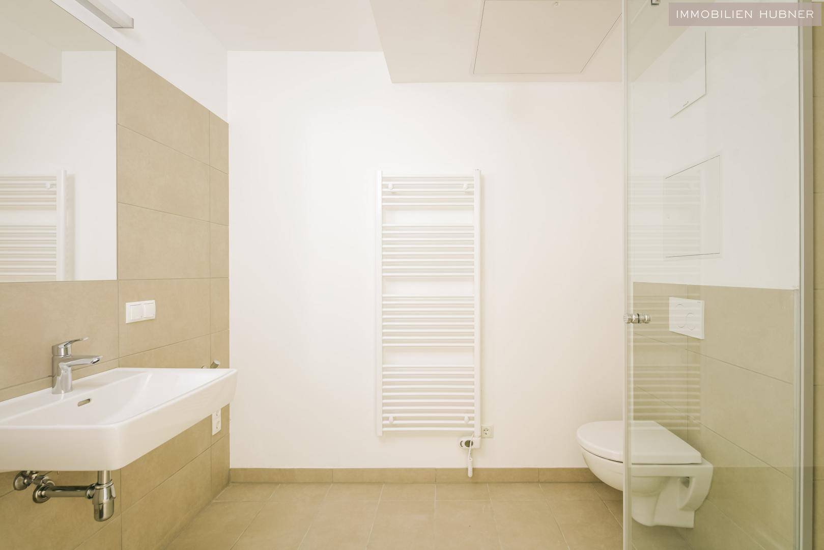 Modernes Badezimmer mit Dusche, WC, Waschbecken und beheiztem Handtuchhalter.