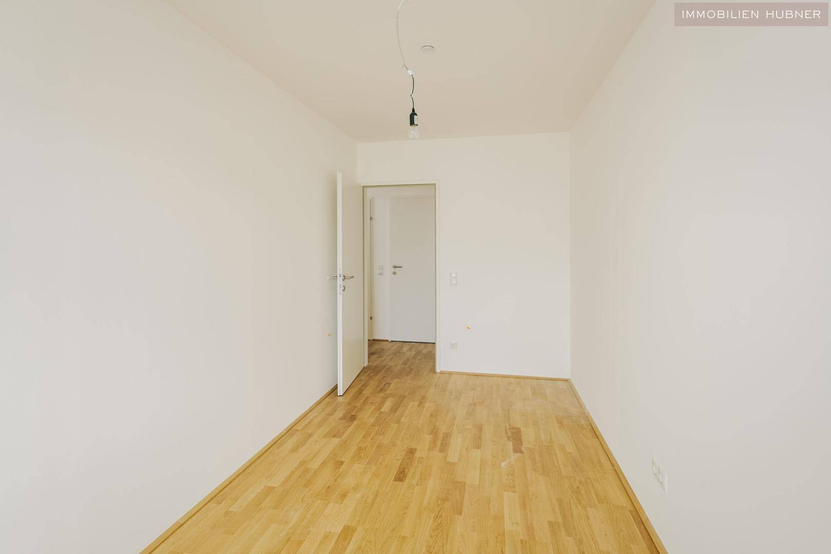 Leeres Schlafzimmer mit hellem Parkettboden und weiß gestrichenen Wänden.