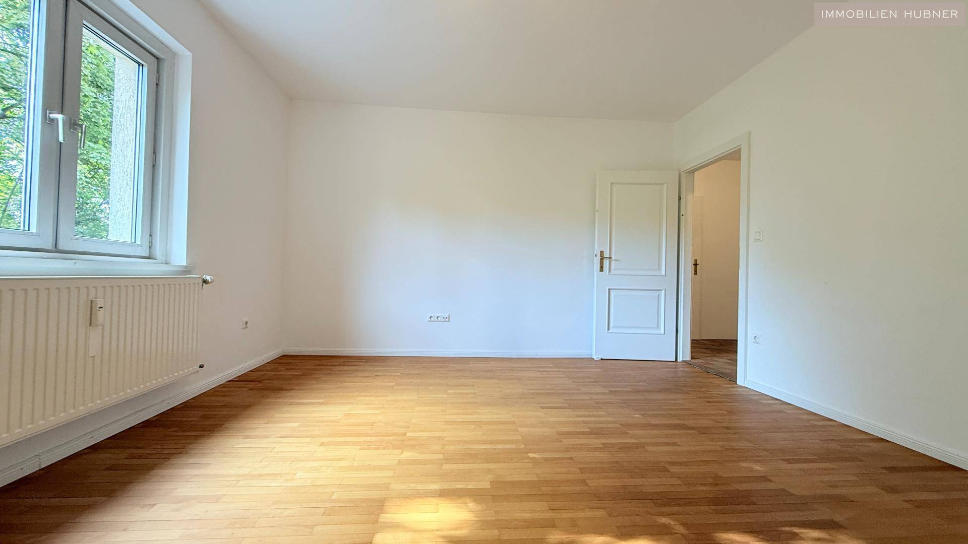 Helles Zimmer mit Parkettboden und Fenster mit Blick ins Grüne.