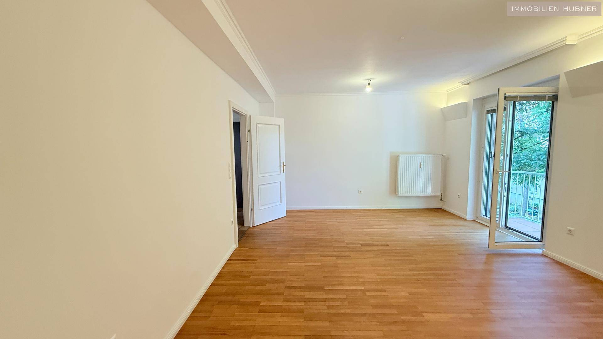 Helles Wohnzimmer mit Parkettboden und Zugang zu einem Balkon.