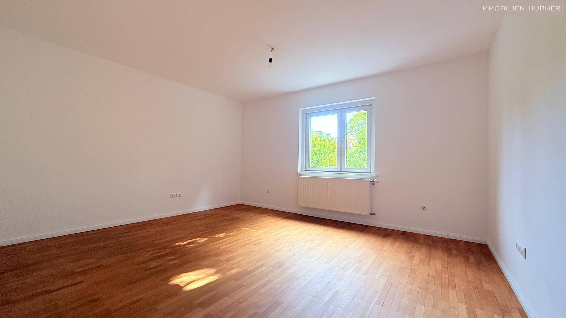 Helles Schlafzimmer mit Parkettboden und großem Fenster.