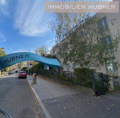 Straßenansicht eines Gebäudes mit Werbebanner und parkenden Autos.
