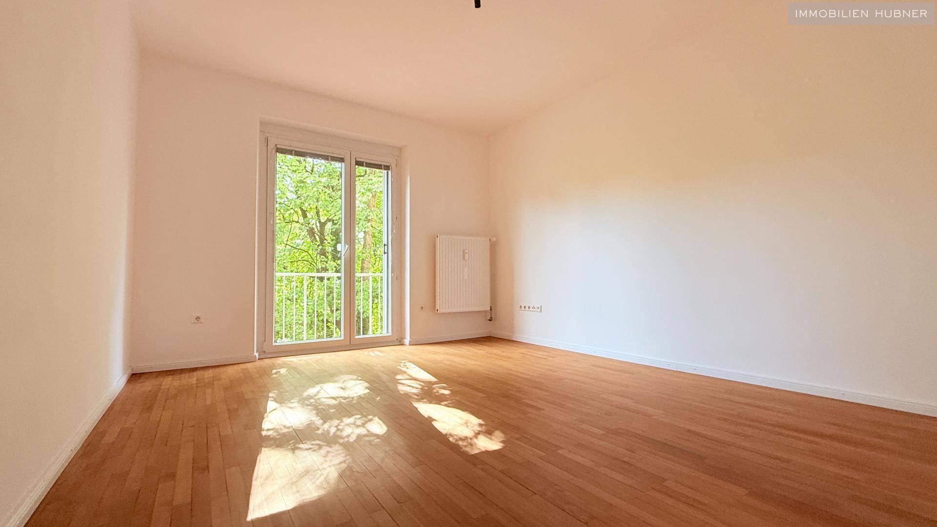 Geräumiges Wohnzimmer mit Parkettboden und Zugang zum Balkon.