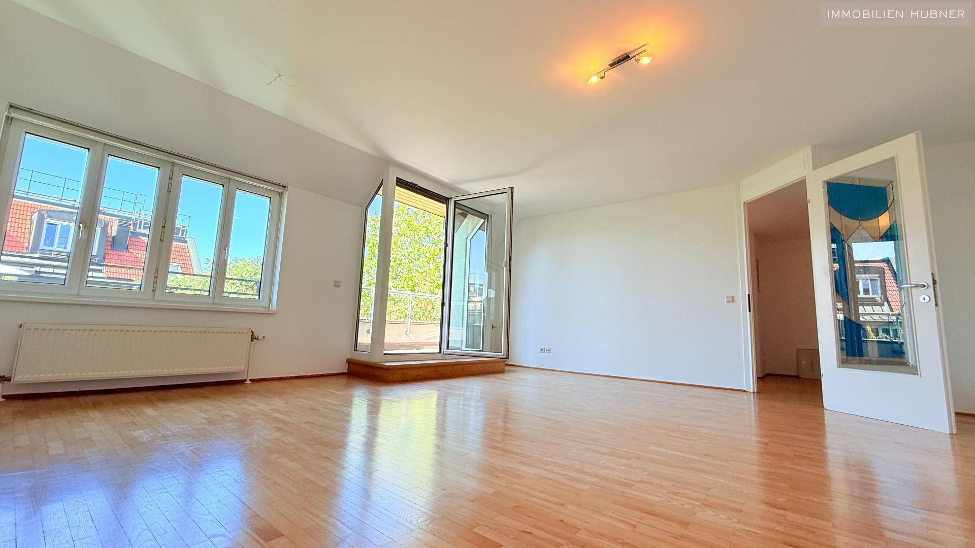 Helles Wohnzimmer mit Parkettboden und Zugang zu einem Balkon, bietet viel natürliches Licht.