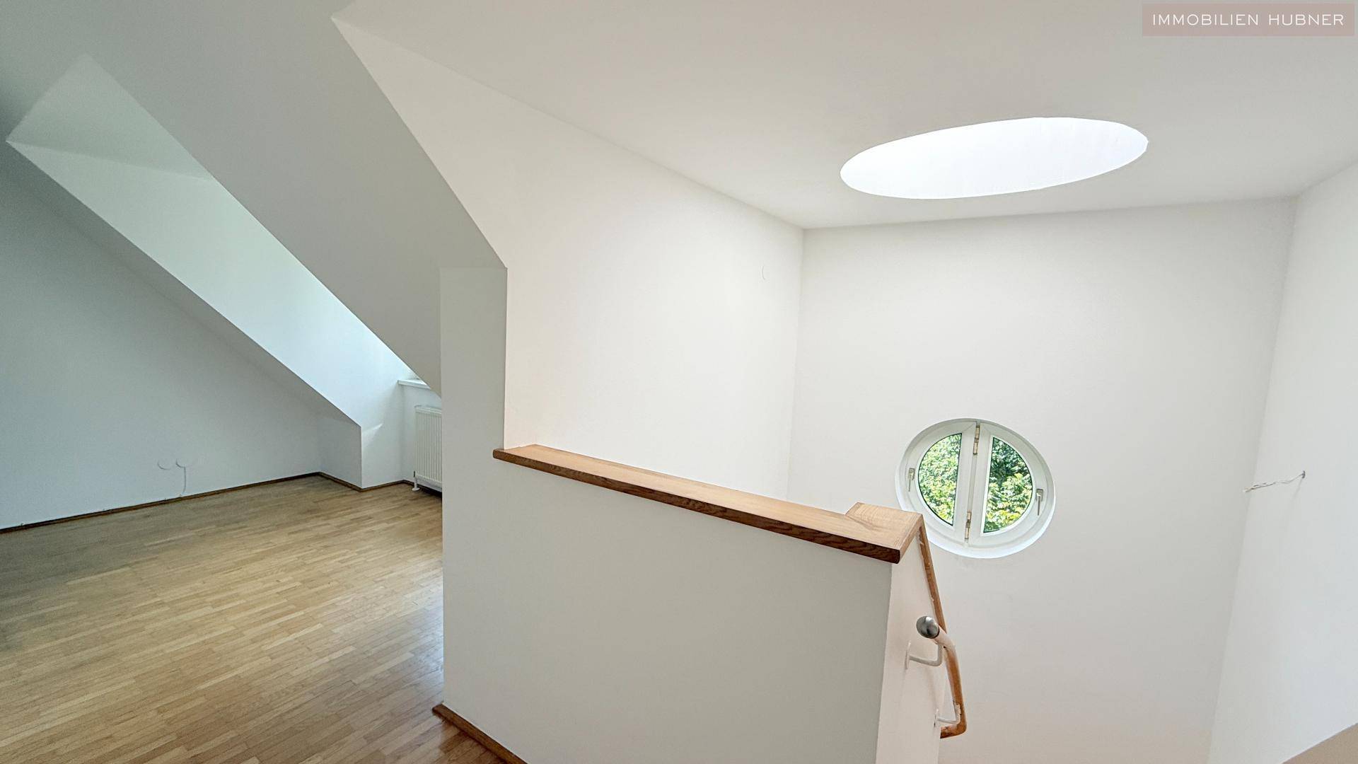 Heller Treppenaufgang mit Dachschräge, Oberlicht und rundem Fenster, das viel Licht spendet.