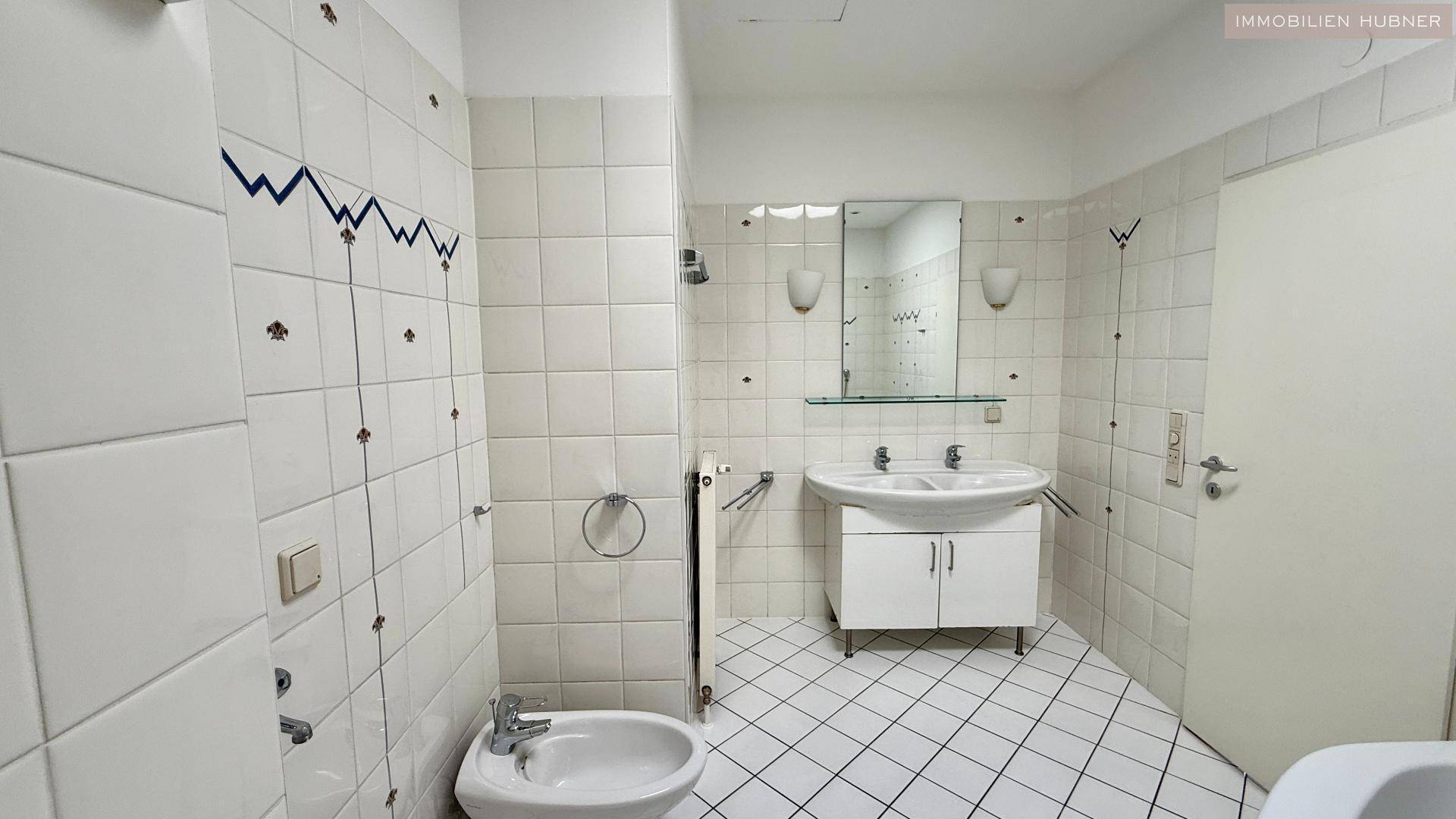 Badezimmer mit Doppelwaschbecken, Bidet und weißen Fliesen, hell und geräumig.