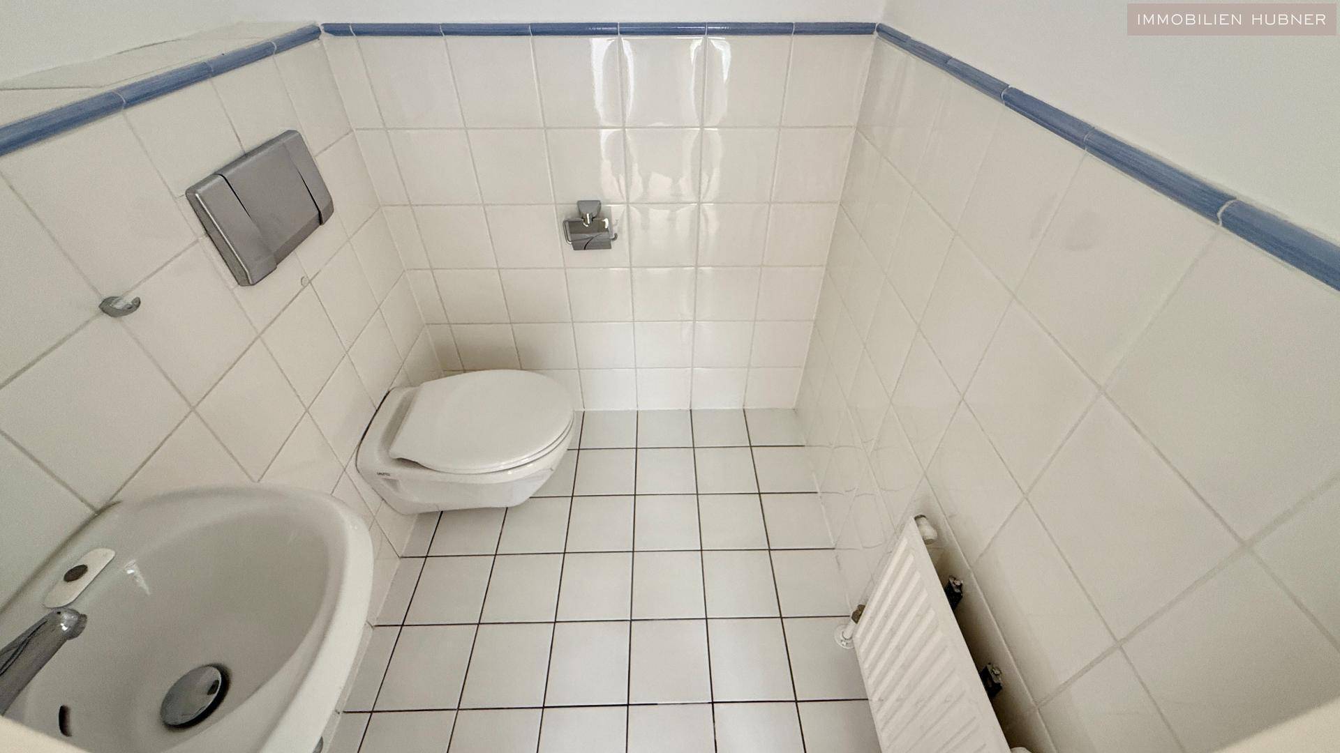 Kleines Gäste-WC mit weißen Fliesen und einem Waschbecken, funktional und sauber.