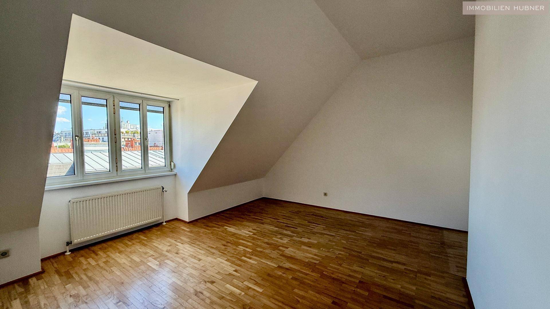 Helles Dachgeschosszimmer mit Holzboden und schrägen Wänden, bietet eine gemütliche Atmosphäre.