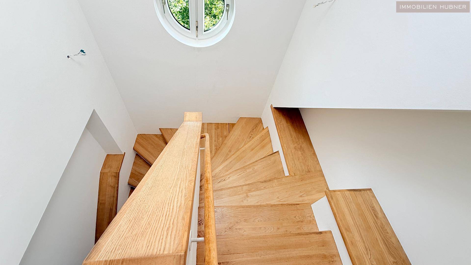 Holztreppe mit Geländer und rundem Fenster, das natürliches Licht in den Treppenbereich bringt.