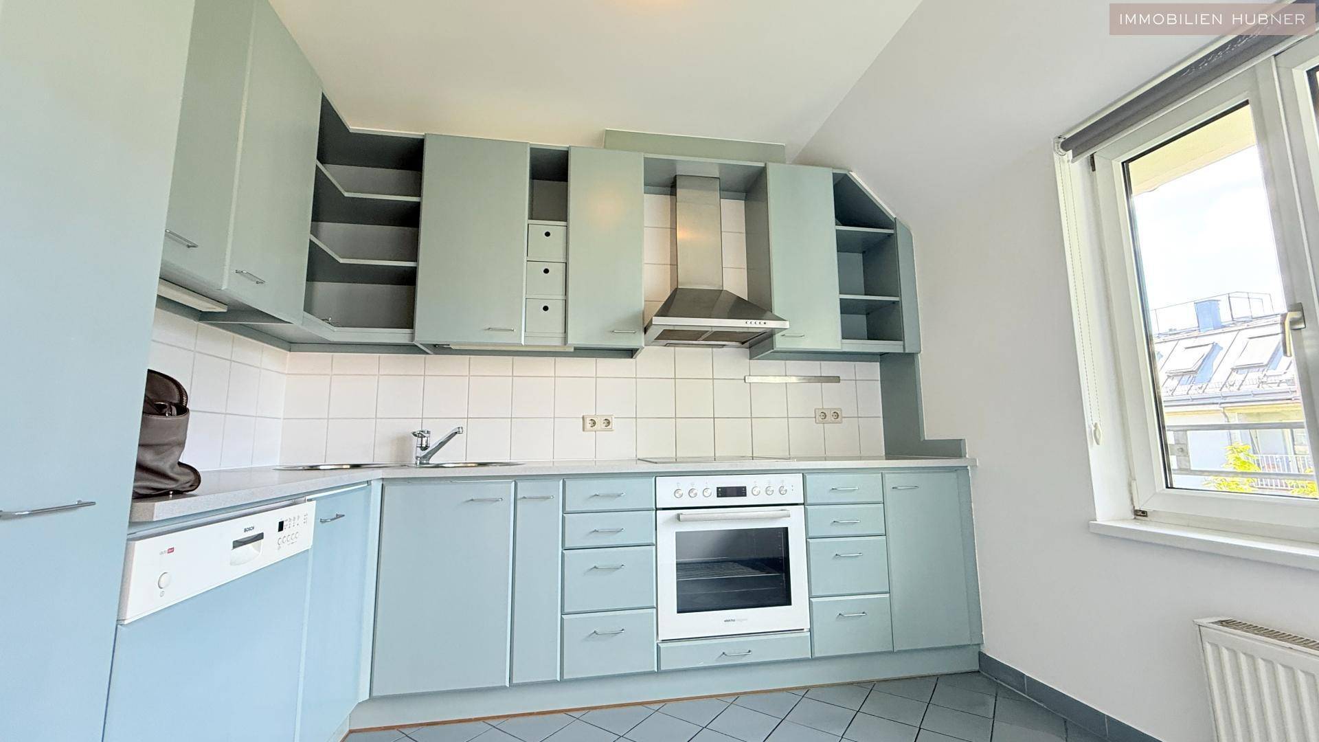 Küche mit hellblauen Einbauschränken, Fliesenboden und Fenster, bereit zur Nutzung.