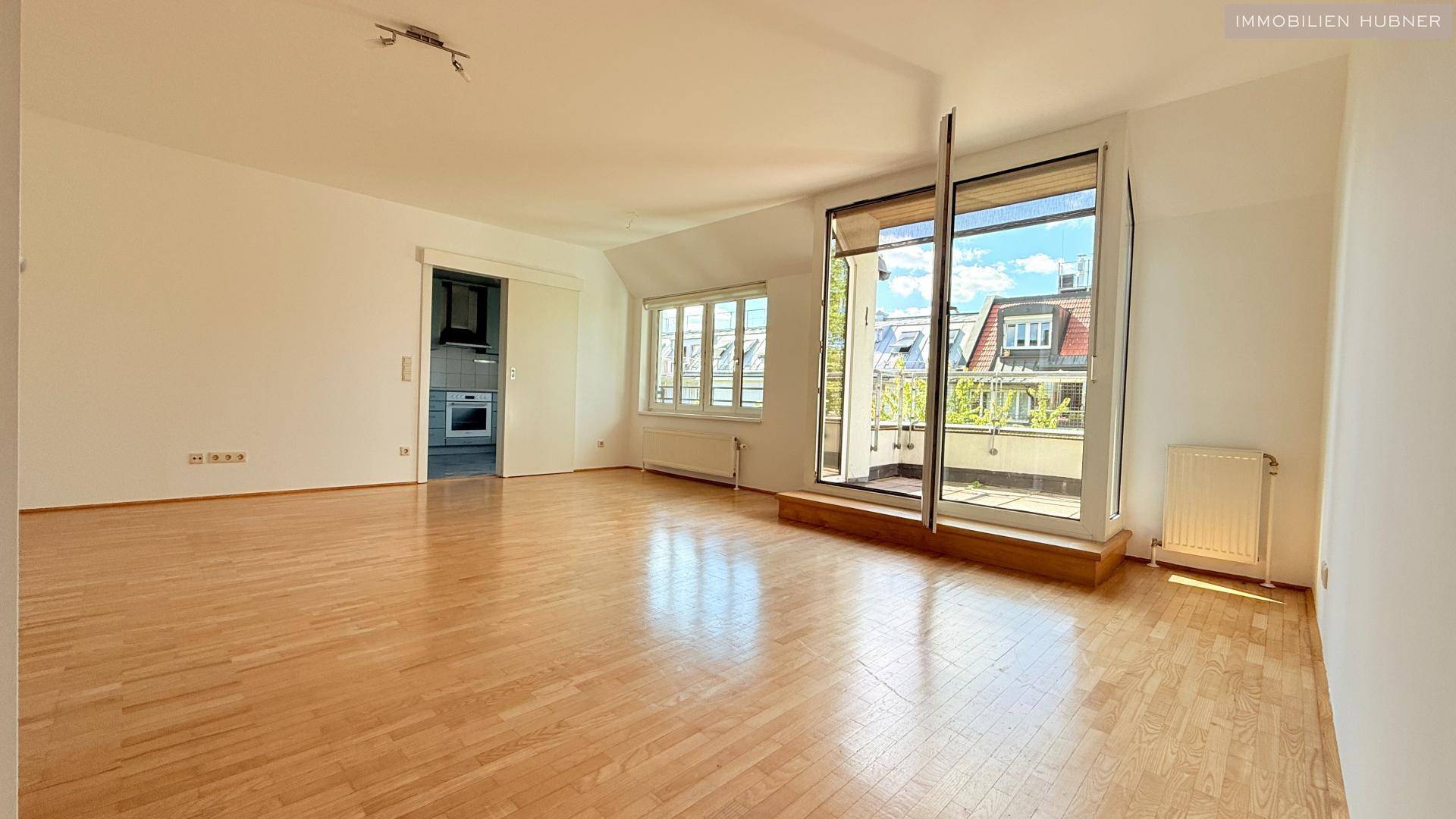 Geräumiges Wohnzimmer mit Holzboden und Schiebetür zur Küche, hell und einladend.