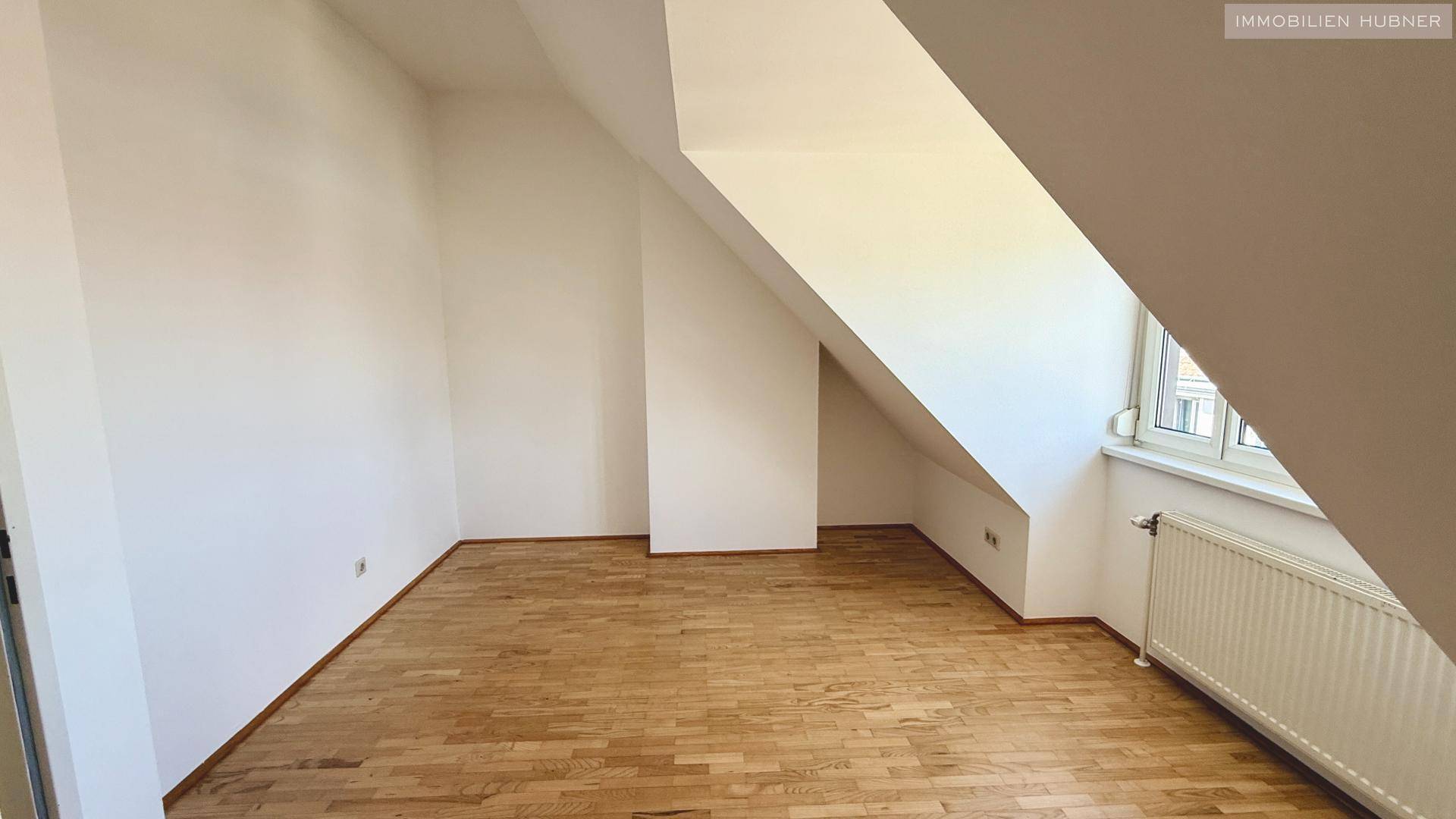 Dachgeschosszimmer mit Holzboden und schrägen Wänden, bietet eine einzigartige Raumgestaltung.