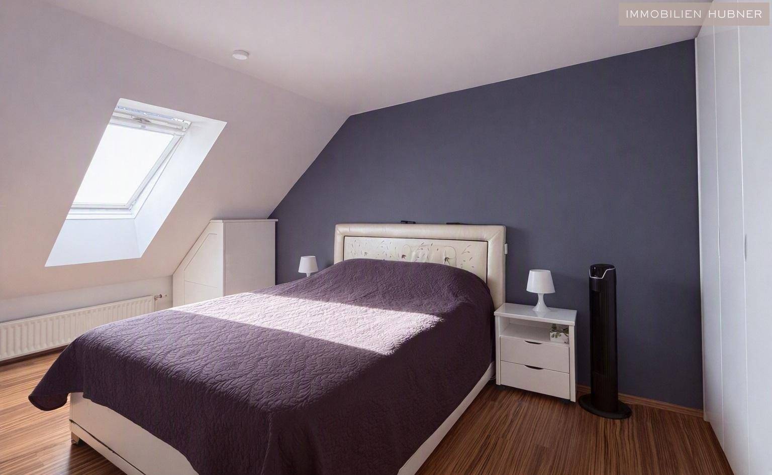 Gemütliches Schlafzimmer mit Doppelbett, dunkler Akzentwand und einem Dachfenster für natürliches Licht.