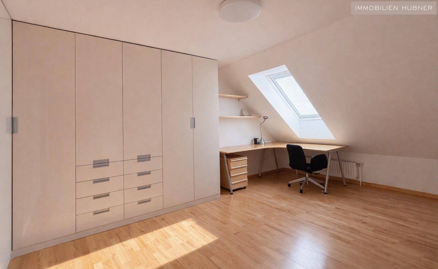 Helles Schlafzimmer mit praktischen Einbauschränken, Schreibtisch unter einem Dachfenster und Holzboden.