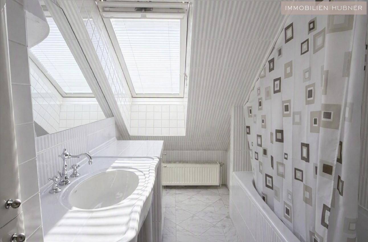 Helles Badezimmer mit Badewanne, Einzelwaschbecken und zwei Dachfenstern, die viel Tageslicht spenden.