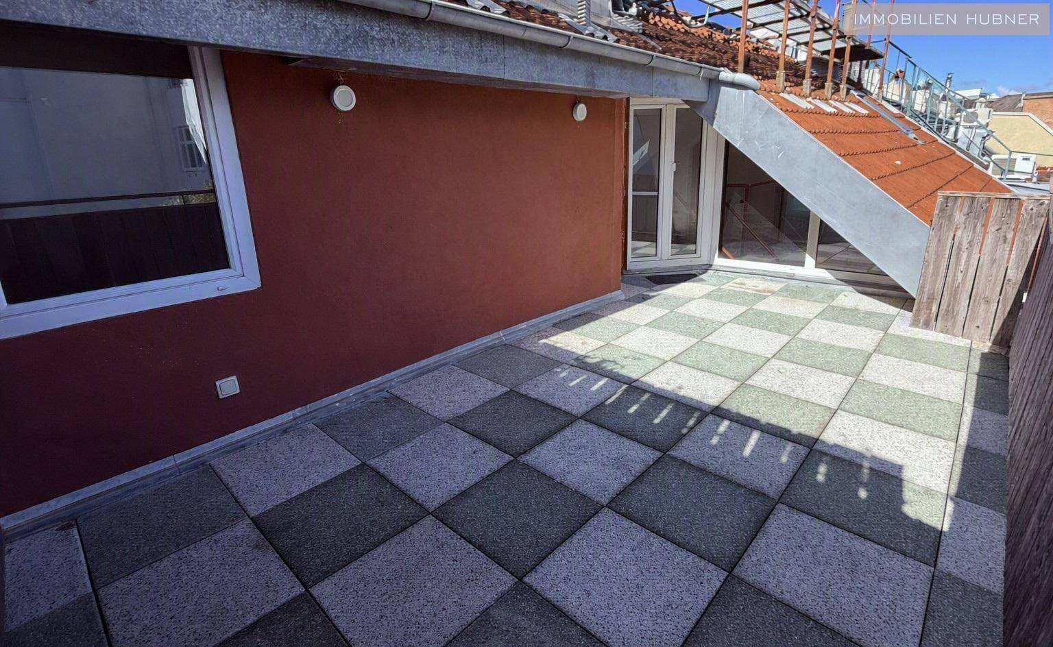 Terrasse mit Zugang zum Innenbereich und einer roten Fassadenwand, bietet Platz für Entspannung im Freien.