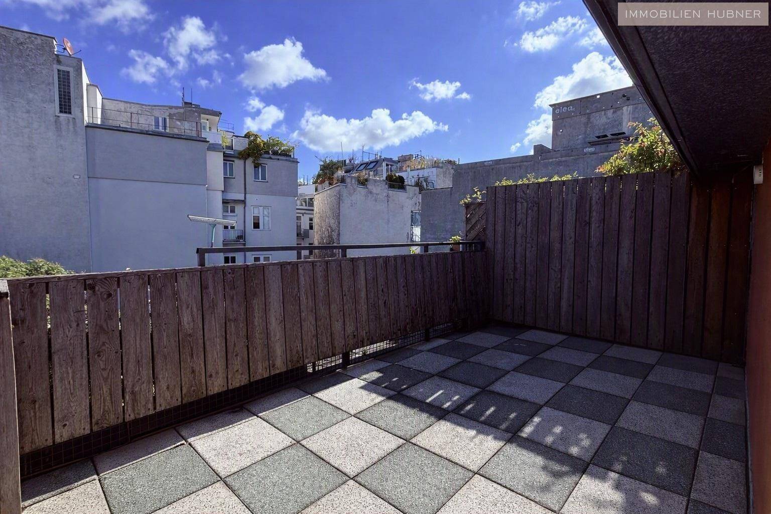 Weitläufige Terrasse mit Holzsichtschutz und Blick auf die umliegenden Dächer und den blauen Himmel.