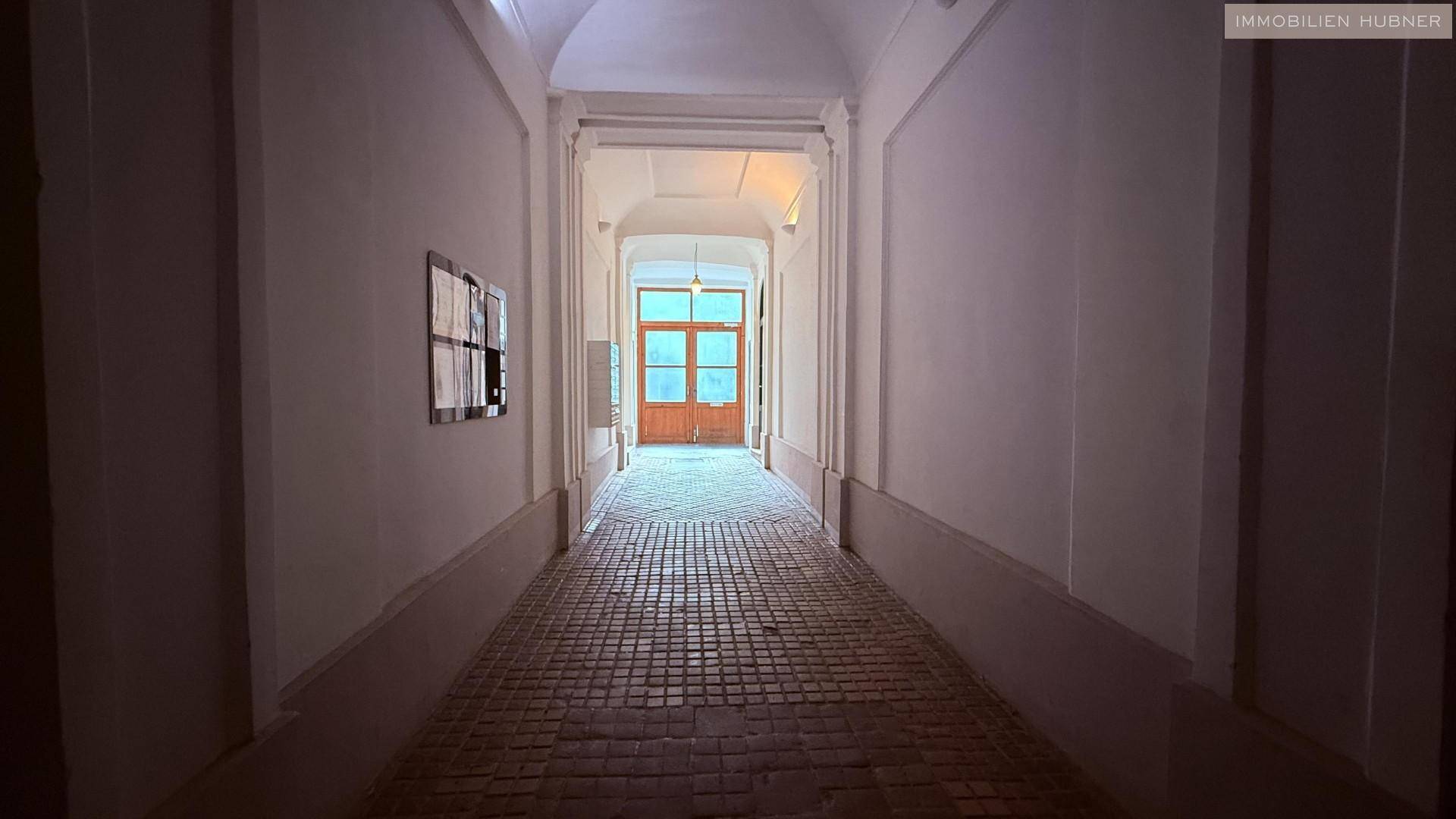 Langer, schmaler Flur mit Ziegelmusterboden und einem gewölbten Deckenbereich, der in die Ferne führt.
