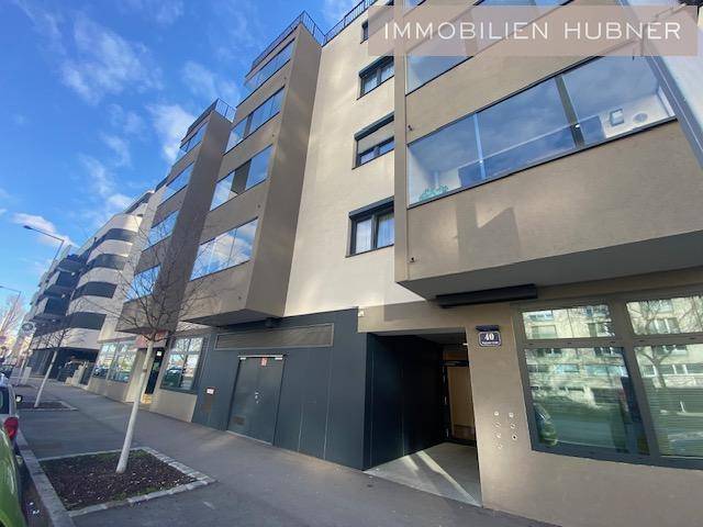 Moderne Gebäudefassade mit großen Fenstern und Eingangsbereich an einer Straße.