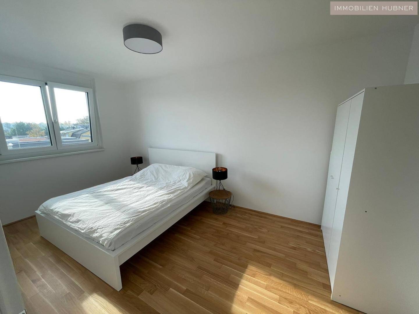 Helles Schlafzimmer mit Holzboden, großem Fenster und modernem Bett.