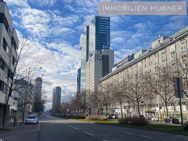 Stadtansicht mit modernen Hochhäusern und belebter Straße unter blauem Himmel.