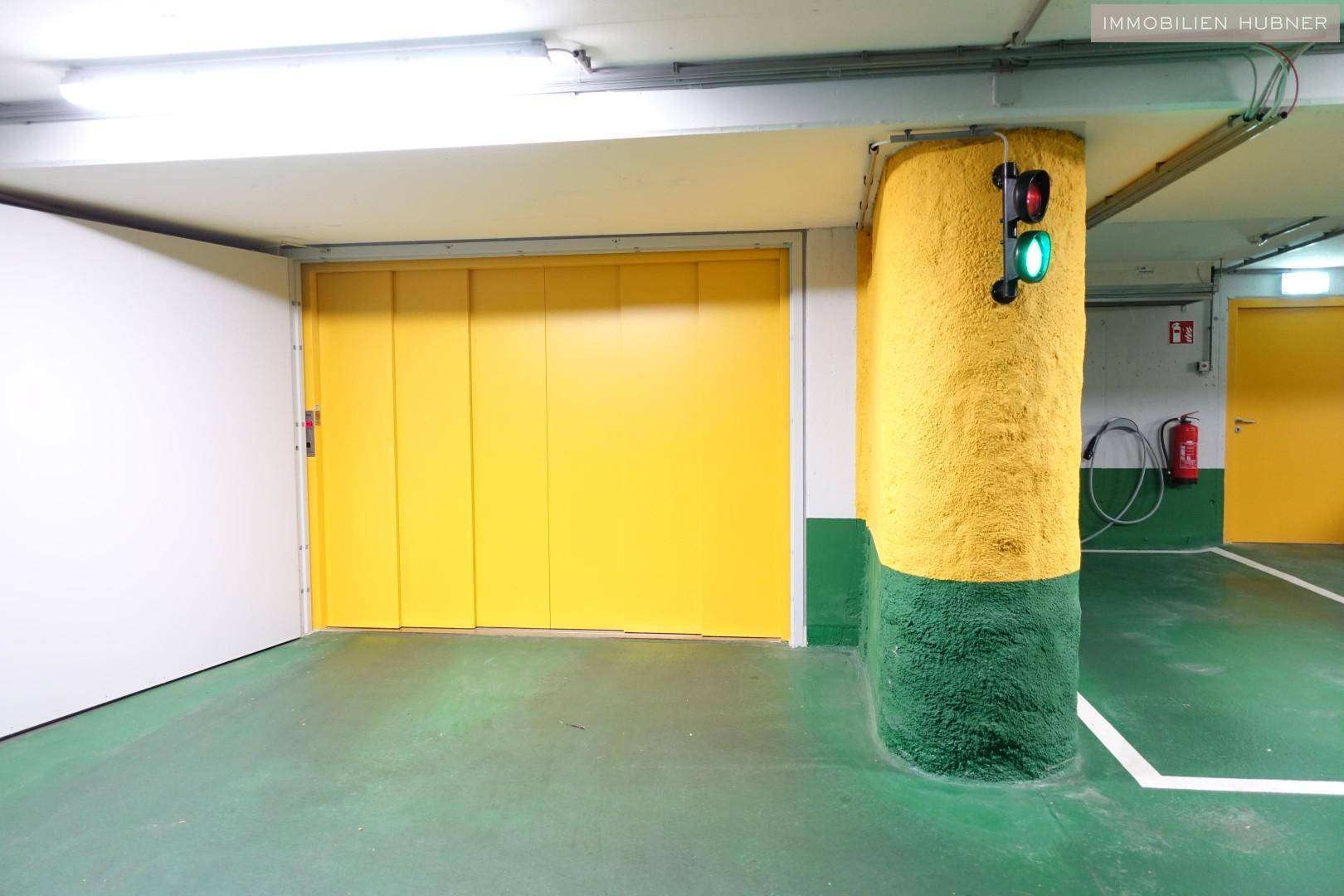 Tiefgaragenbereich mit gelber Aufzugstür, farbigen Säulen und Sicherheitsausrüstung an der Wand.