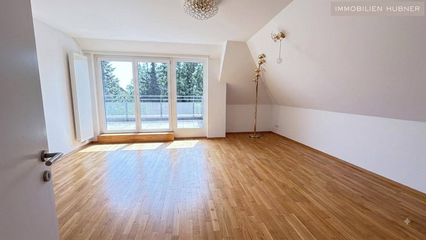 Heller Raum mit Holzparkettboden, Dachschrägen und großen Fenstertüren, die zu einem Balkon führen.