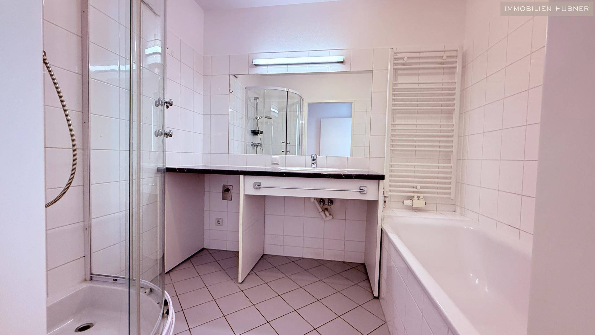 Gefliestes Badezimmer mit Duschkabine, Badewanne, Einzelwaschbecken und beheiztem Handtuchhalter.