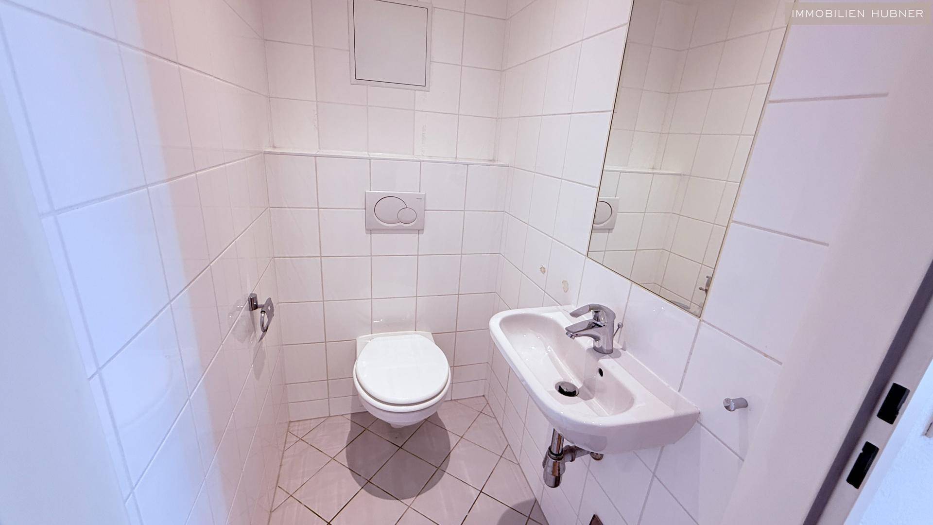 Kleines Gäste-WC mit weißen Fliesen, wandhängendem WC und einem kompakten Waschbecken.