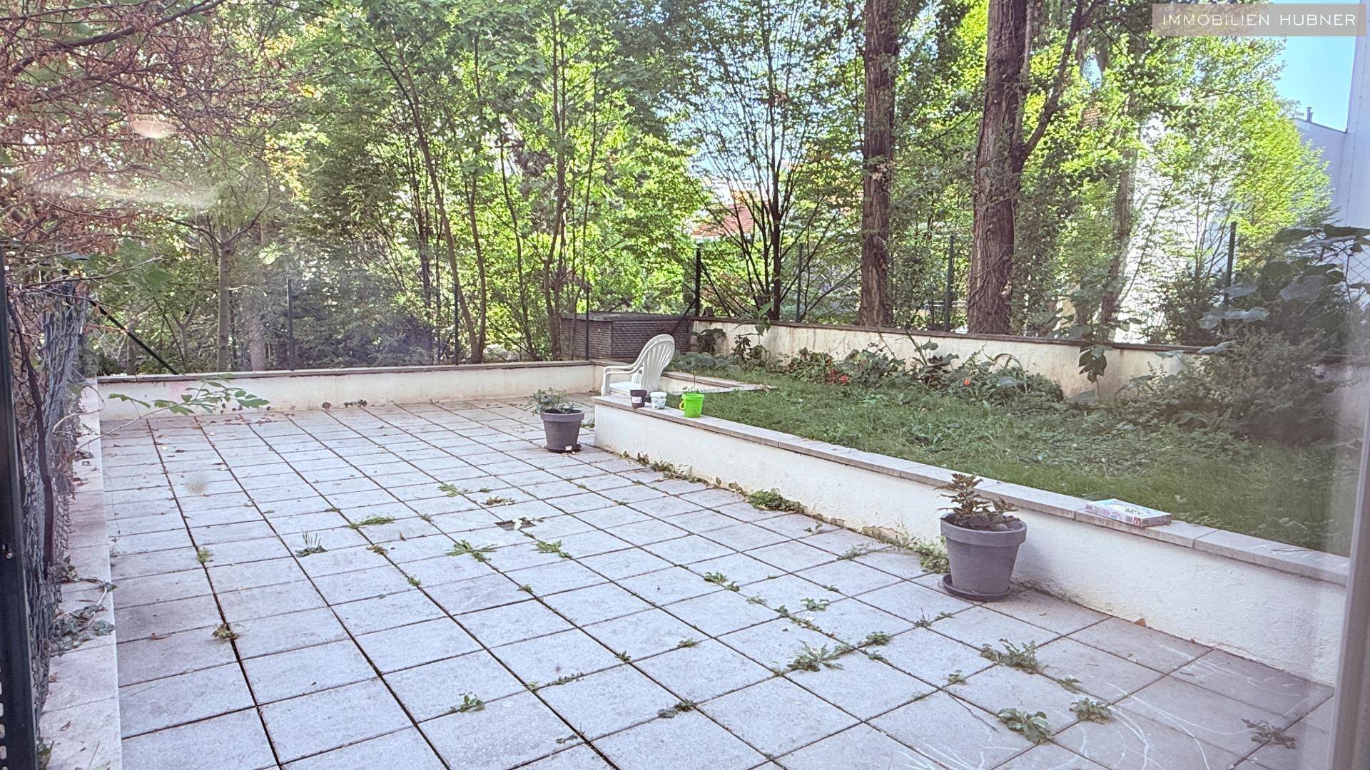 Große gepflasterte Terrasse mit angrenzendem Gartenbereich und altem Baumbestand.