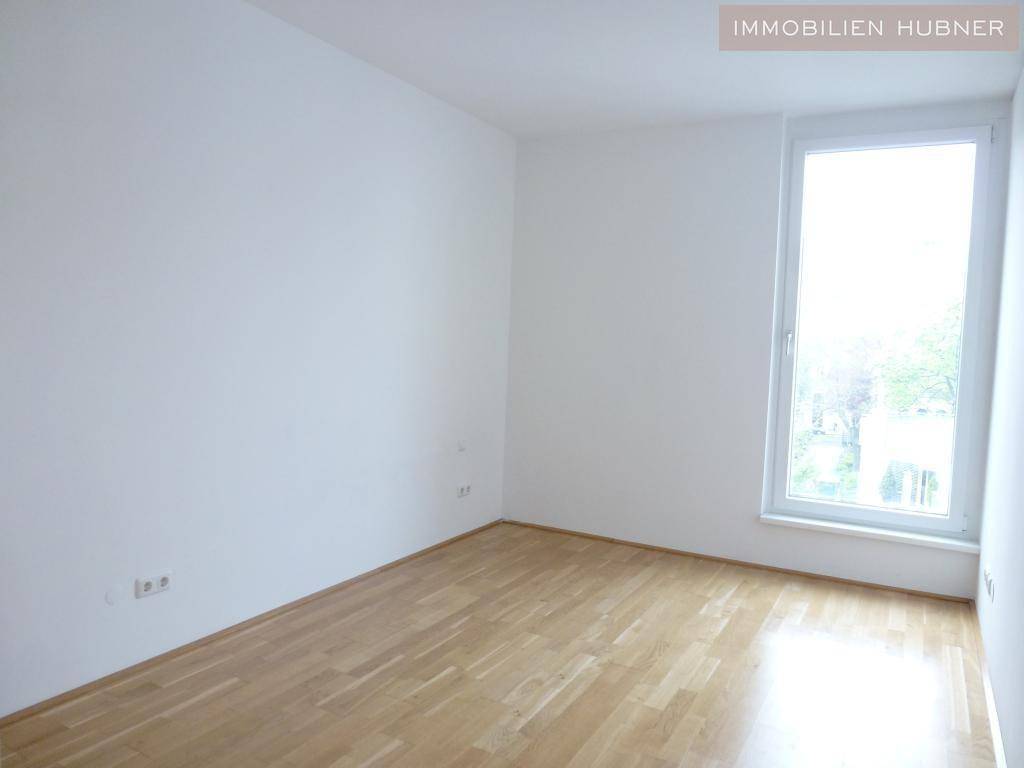 Leeres Zimmer mit hellem Parkettboden und großem Fenster für viel Tageslicht.